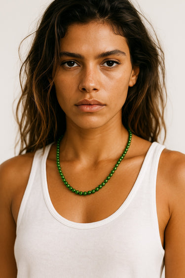 Woman wearing a white tank top and green necklace against a plain background