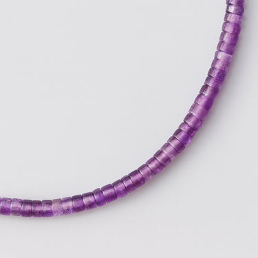 A macro close-up view highlighting the unique disc-shaped amethyst heishi beads and their natural purple color variations.
