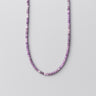 A studio shot of a 4mm amethyst round bead necklace curved against a neutral background, highlighting the uniform shape and deep violet color of the beads.
