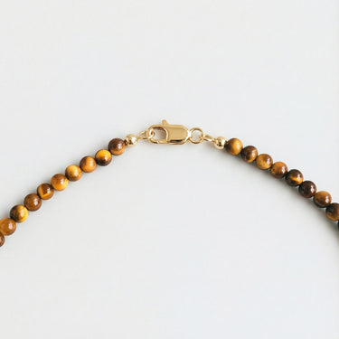 A macro close-up view of 4mm Tiger's Eye beads finished with a high-polish gold lobster clasp.
