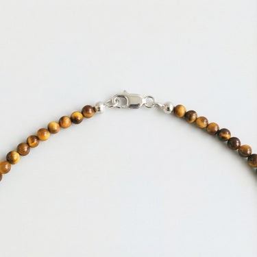A macro close-up view of 4mm Tiger's Eye beads finished with a high-polish silver lobster clasp.
