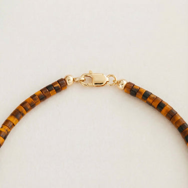 A macro close-up view of 4mm Tiger's Eye heishi beads finished with a high-polish gold lobster clasp.

