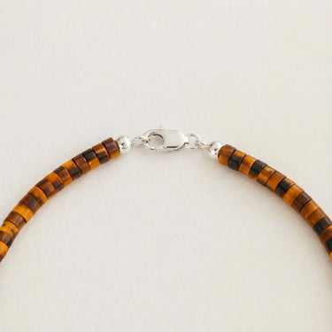 A macro close-up view of 4mm Tiger's Eye heishi beads finished with a high-polish silver lobster clasp.
