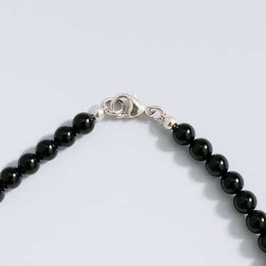 Black beaded bracelet with silver clasp on a light gray background