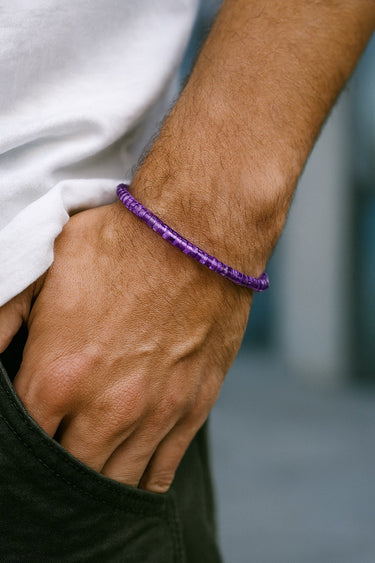 Close-up of a hand wearing a purple bracelet with a blurred background