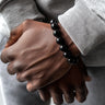 Close-up of two hands clasped together with a black beaded bracelet on a neutral background