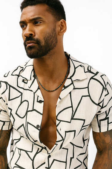 Man wearing a white shirt with black geometric patterns and a necklace.