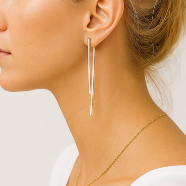 Close-up of a woman wearing silver earrings and a gold necklace on a plain background