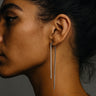 Close-up of a woman wearing long, dangling sterling silver earrings against a dark background
