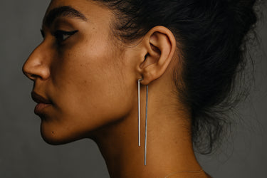 Close-up of a woman wearing long, dangling sterling silver earrings against a dark background