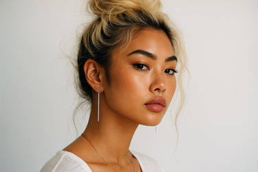 Woman with styled hair and earrings, minimal silver bar drop earrings with sleek vertical design for everyday wear against a plain background. 
