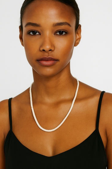 Woman wearing a black top and white necklace against a plain background