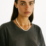 Woman wearing a dark gray t-shirt and pearl necklace against a white background