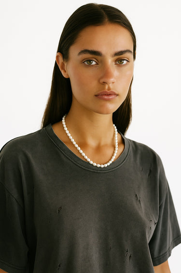Woman wearing a dark gray t-shirt and pearl necklace against a white background