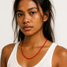 Woman wearing a white tank top and red necklace against a plain background