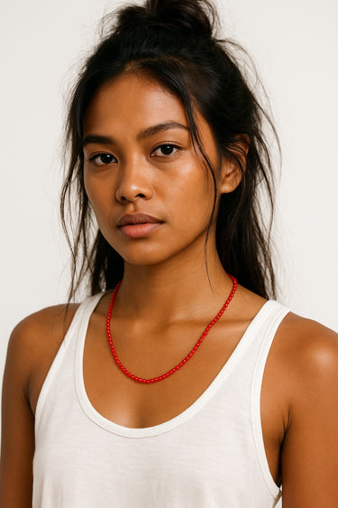 Woman wearing a white tank top and red necklace against a plain background