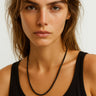 Woman wearing a black tank top and necklace against a plain background