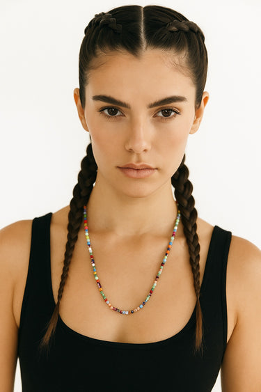 Woman with braided hair wearing a black tank top and colorful necklace on a white background