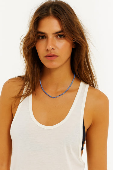 Woman wearing a white tank top and blue necklace on a plain background