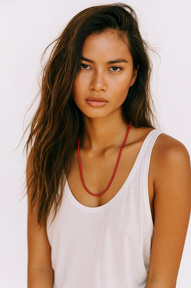 Woman wearing a white tank top and red necklace against a white background