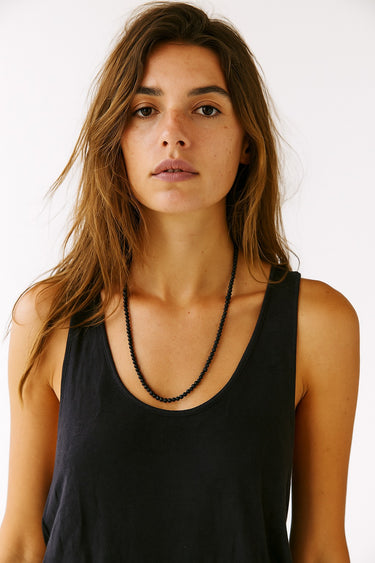 Woman wearing a black tank top and necklace against a white background