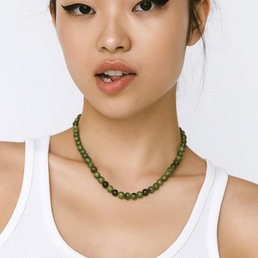Woman wearing a white tank top and green beaded necklace against a white background