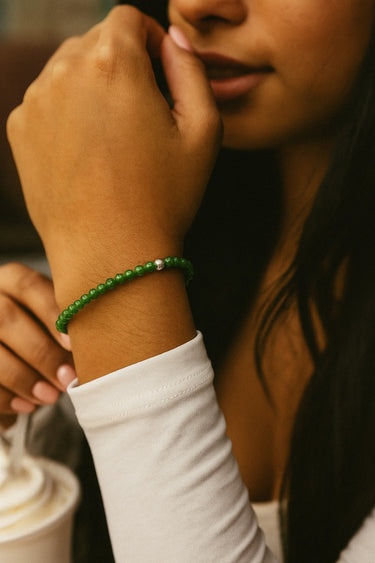 Close-up of a woman wearing a 4mm green jade bracelet with one sterling silver accent with a blurred background