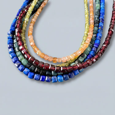 Faceted gemstone bead necklaces in multiple colors including blue, red, yellow and green arranged in layered flat lay