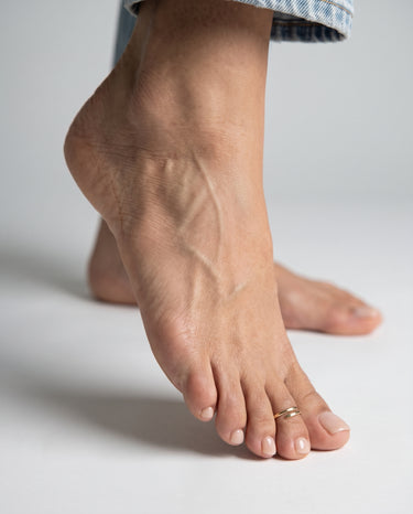 Close-up of a foot wearing a gold overlap style toe ring on second toe on a neutral background