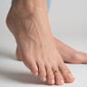 Close-up of a foot wearing a gold overlap style toe ring on second toe on a neutral background