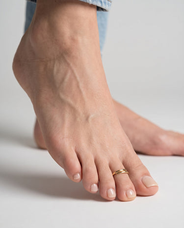Close-up of a foot wearing a gold overlap style toe ring on second toe on a neutral background