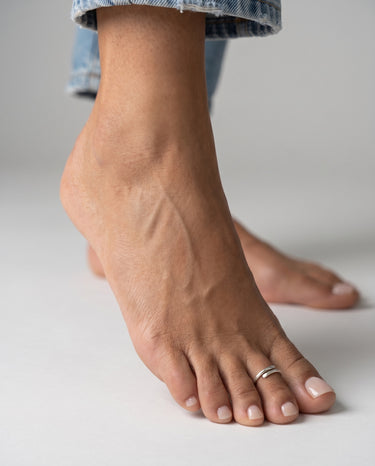 Close-up of a foot with a sterling silver overlap style toe ring on the second toe on a neutral background.