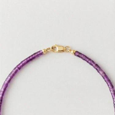 A close-up view of purple amethyst heishi beads finished with a high-polish gold lobster clasp.
