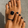 Close-up of black toe ring on the big toe of feet with black nail polish on toes against a neutral background