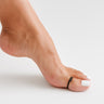 Close-up of a foot with a black toe ring on a light gray background. Arch visibile side angle view of black overlap big toe ring. 