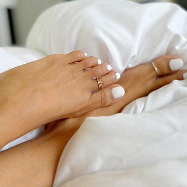 model wearing 3 stacked toe rings, sterling silver, 14k rose gold, and gold-filled on a soft background