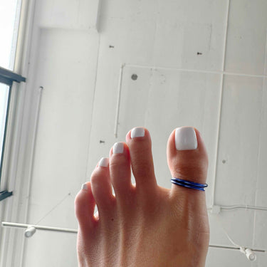 Dark blue anodized aluminum big toe ring on toes while standing on stone surface — deep color tone and open-band comfort.