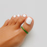Close-up of a foot with white nail polish and a green bandage on a light gray background