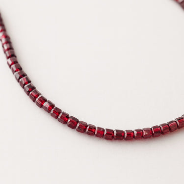 A curved segment of deep red faceted Garnet cube beads showing light refraction on the faceted surfaces.

