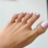 Close-up of a foot wearing a gold big toe overlap ring with pink nail polish on a neutral background