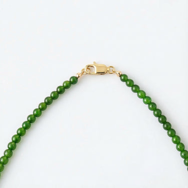 A macro view of green jade beads connected to a high-polish gold lobster clasp against a white background.
