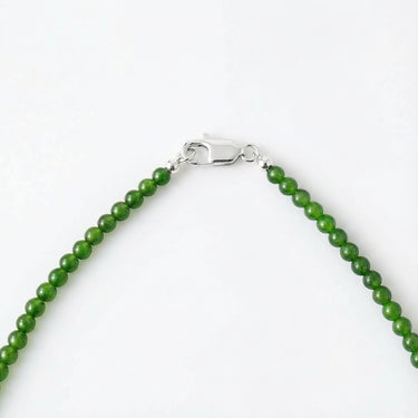 A macro view of green jade beads connected to a high-polish silver lobster clasp against a white background.
