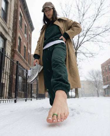 Person wearing a beige coat and green pants standing in the snow.