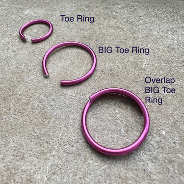 Hot pink anodized aluminum toe ring displayed on concrete surface — bright anodized finish from the COLORS Collection.