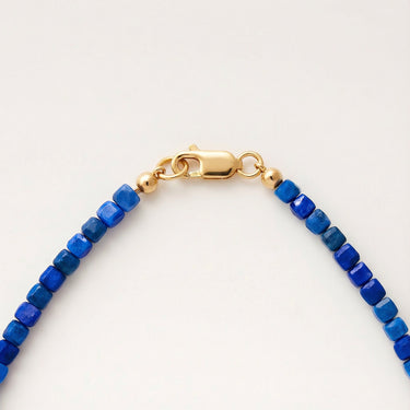 Macro view of blue faceted cube beads finished with a high-polish gold lobster clasp.
