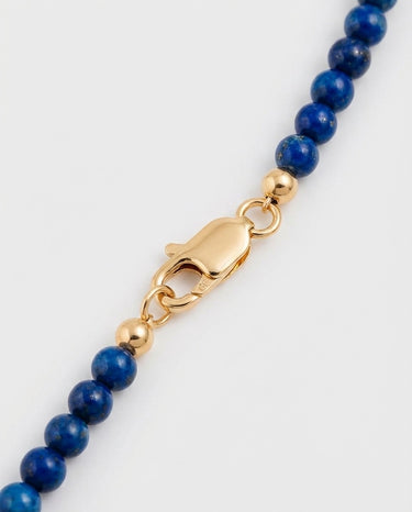 A macro close-up of 4mm blue gemstone beads finished with a high-polish gold lobster clasp and gold accent beads.
