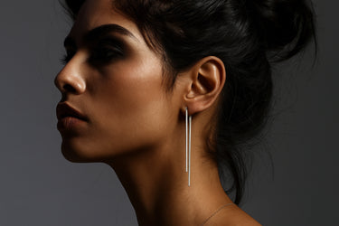 Side view of silver double drop earrings with modern layered design. Close-up of a woman wearing a silver earring against a dark background