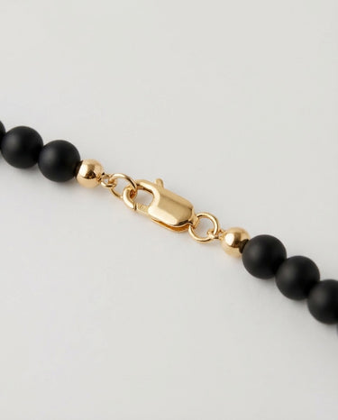 A macro close-up view of matte black onyx beads finished with a high-polish 14K gold-filled lobster clasp.
