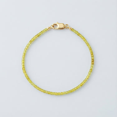 A 2mm faceted Peridot cube bead bracelet featuring vibrant lime-green tones and a high-polish gold lobster clasp.
