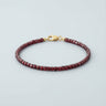 A 3mm faceted Garnet cube bead bracelet featuring deep burgundy tones and a high-polish gold lobster clasp, displayed against a light grey background.
